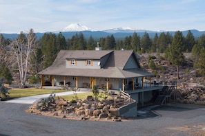 A two-story house with a covered porch, a stone retaining wall, and a view of a mountain range. - Mountain View Retreat - 3Bed - 2.5 Bath on 17acres (Bend)