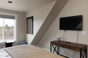 A bedroom with a bed, a bedside table, a TV mounted on the wall, and a window with a view of trees. - Mountain View Retreat - 3Bed - 2.5 Bath on 17acres (Bend)