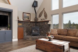 A living room with a stone fireplace, a sofa, a coffee table, and a television. - Mountain View Retreat - 3Bed - 2.5 Bath on 17acres (Bend)