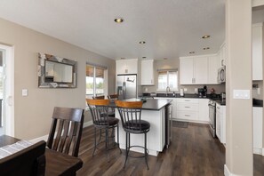 A modern kitchen with white cabinets, a stainless steel refrigerator, and a bar area with stools. - Mountain View Retreat - 3Bed - 2.5 Bath on 17acres (Bend)