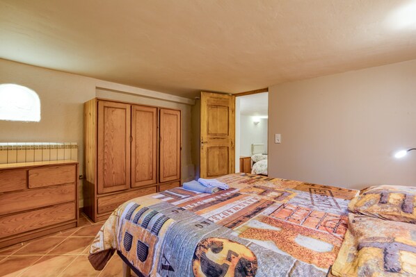 Quarto com uma cama grande, guarda-roupa de madeira e uma porta que dá para outro espaço.