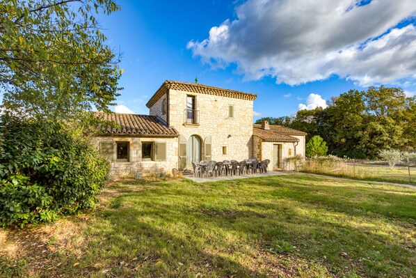 A stone house with a tiled roof, a patio with outdoor furniture, and a well-maintained lawn. - Spacious villa with 25 m pool and spa, mountain view, 20 min from Montpellier (St Mathieu de Tréviers)