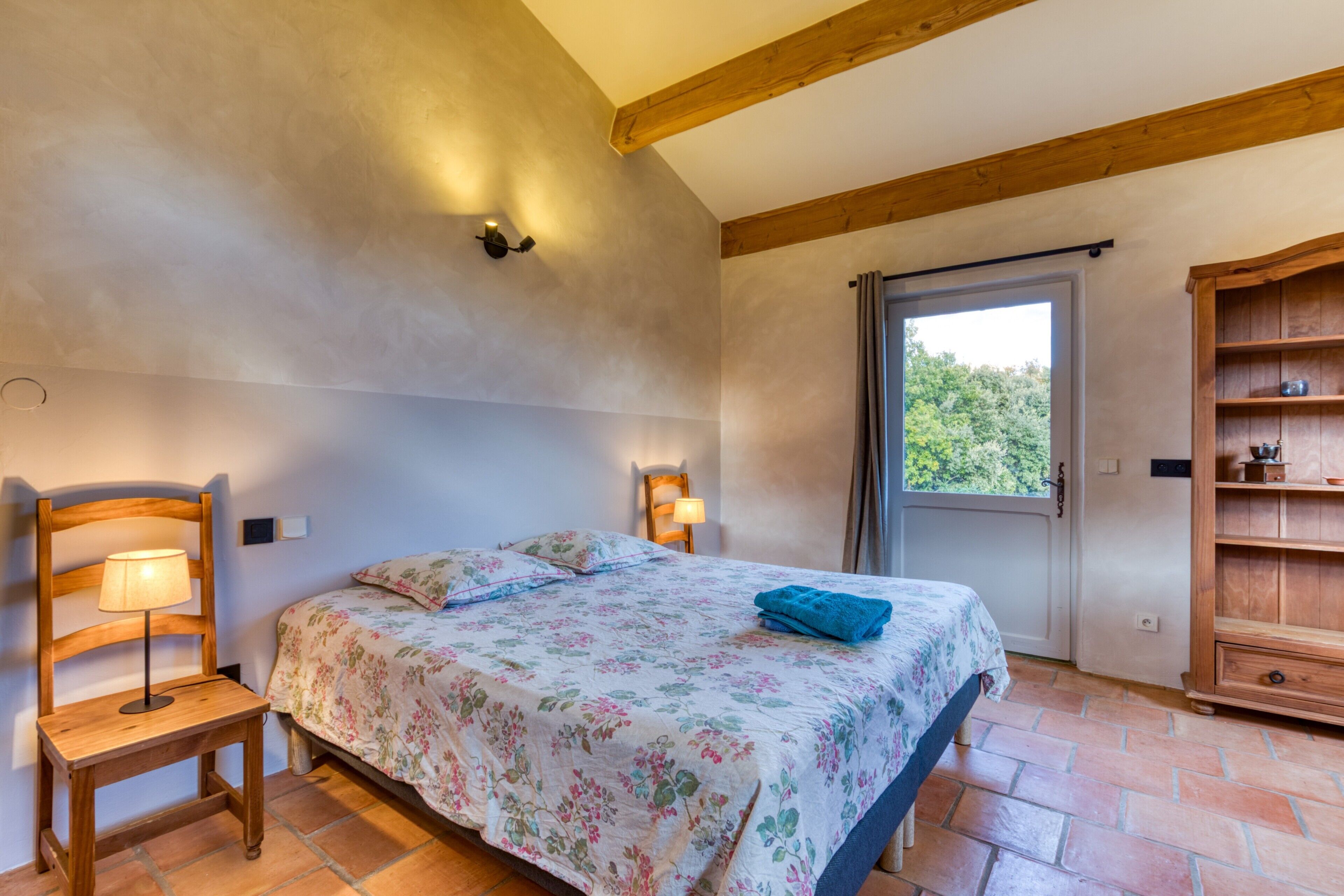 A bedroom with a bed, a wooden chair, a nightstand, a lamp, and a wooden cabinet.