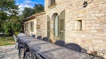 Ein Steinhaus mit einer Pflasterterrasse, einem Tisch und Stühlen, einer Steinmauer und einem Fenster mit Fensterläden.