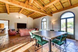 Un vaste espace de vie comprenant une grande table en bois, des fauteuils à revêtement vert, un canapé rouge et un téléviseur.