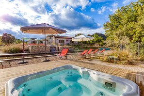 Un bain à remous sur une terrasse en bois, avec des chaises longues et des parasols.