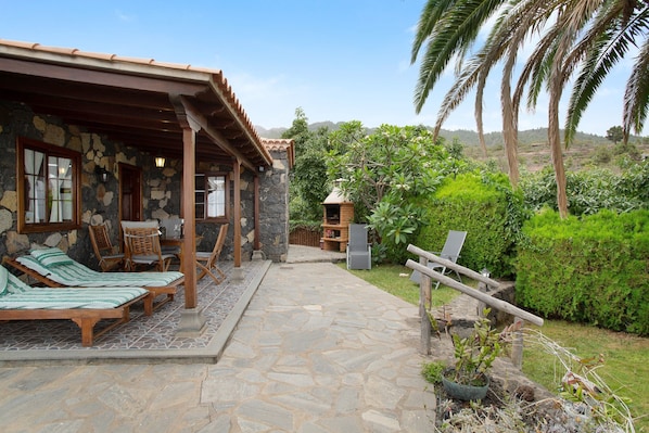 A stone building with a covered patio, outdoor seating, and a view of a lush garden.