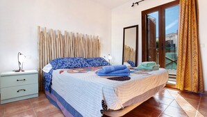 A bedroom with a bed, a nightstand, a mirror, and a view of the outdoors. - Vacation Home 'Villa Charlotte' with Mountain View, Shared Pool and Wi-Fi (La Oliva)