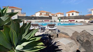 A swimming pool with lounge chairs, a large plant, and buildings with orange roofs. - Vacation Home 'Villa Charlotte' with Mountain View, Shared Pool and Wi-Fi (La Oliva)