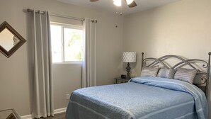 A bedroom with a bed, a nightstand, a lamp, a window with curtains, and a ceiling fan.