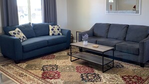 A living room with two dark blue sofas, a coffee table, and a patterned rug.