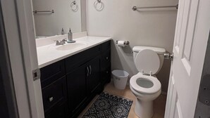 A bathroom with a white sink, black cabinets, a toilet, a trash bin, and a patterned rug.