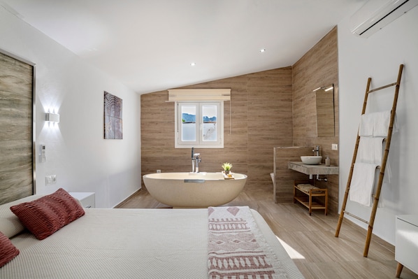 Un dormitorio moderno con una cama grande, una bañera independiente y suelo de madera.