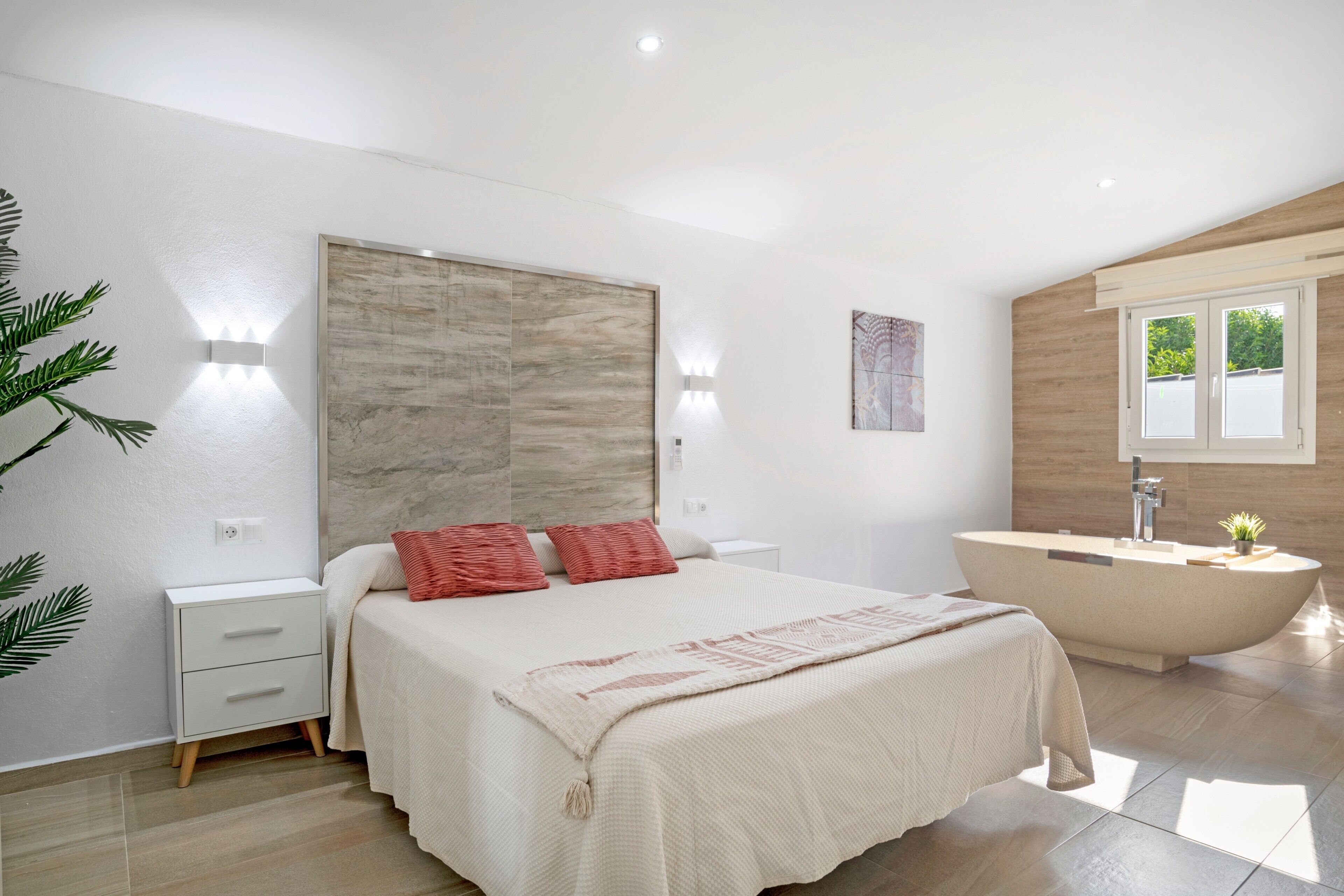 A modern bedroom with a large bed, bedside tables, a built-in bathtub, and a wall-mounted light fixture.