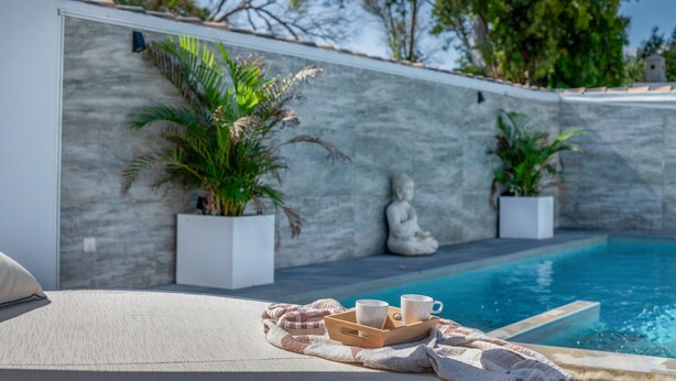 Un espace aménagé au bord de la piscine, avec un fauteuil de relaxation, un plateau avec des tasses et des plantes en pot.
