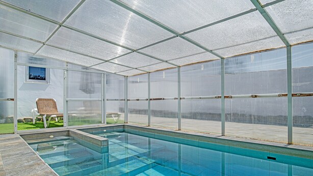 A covered swimming pool with clear glass walls, a bench, and a small window. - Holiday Home 'Casa El Elefante' with Heated Pool, Wi-Fi and Air Conditioning (Vejer)