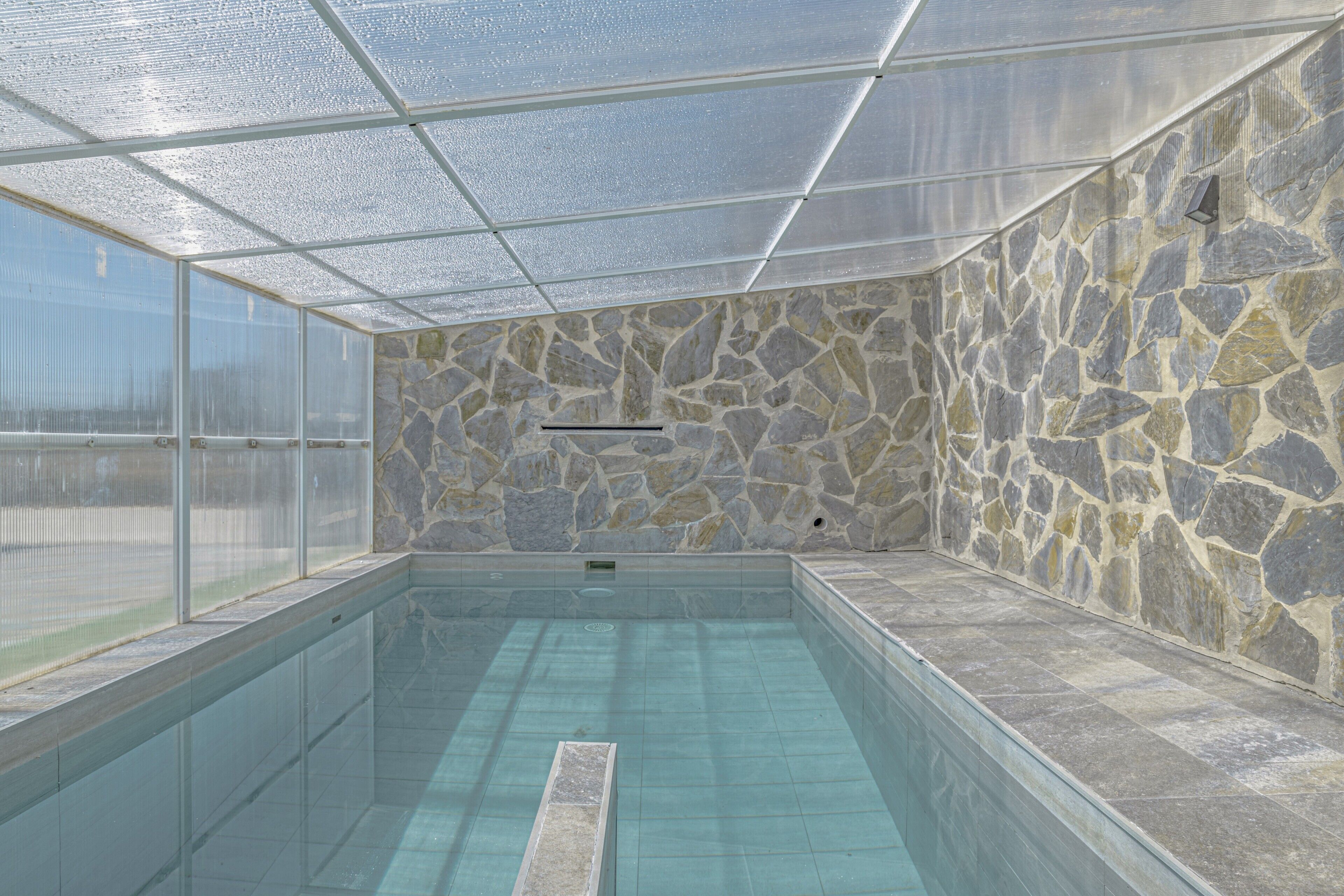 Une piscine avec des murs en pierre et un toit en verre.