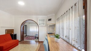 Una sala moderna con un sofá, una mesa de comedor de madera con una planta, y una zona de cocina con una ventana.