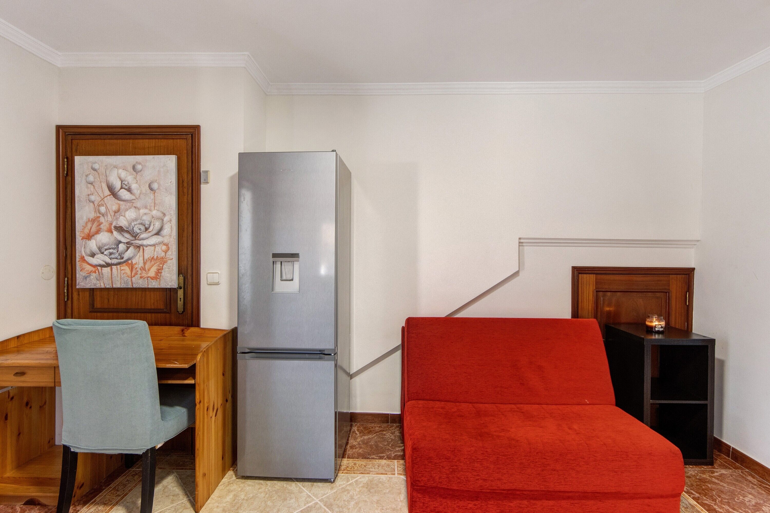 Un espacio habitable compacto con una mesa de madera, una silla, un sofá rojo, un refrigerador y un mueble pequeño.
