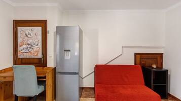 Un espacio habitable compacto con una mesa de madera, una silla, un sofá rojo, un refrigerador y un mueble pequeño.