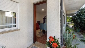 Un espacio al aire libre techado con una puerta que da a un ambiente interior, una ventana y plantas en macetas.