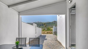 Eine moderne Außenpatio mit Tisch und Stühlen, einem Topfpflanzen und Blick auf eine Hügelkuppe.