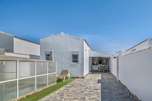 A narrow stone pathway leading to a white building with a small garden area and a chair.