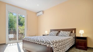 Un dormitori amb un llit, una tauleta de nit, una làmpada, una porta corredissa de vidre i un aparell d'aire condicionat.
