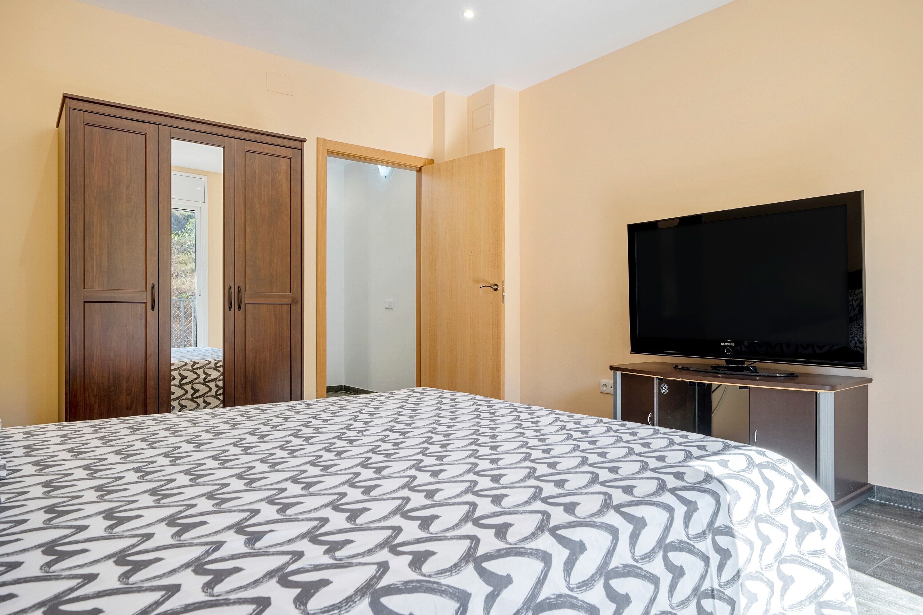 A bedroom with a bed, a television, a wardrobe, and a door leading to another room.