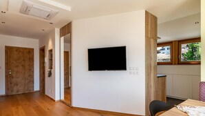 Een moderne kamer met een flatscreen televisie aan de muur, houten vloer en een eethoek met een tafel en stoelen.
