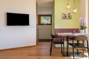 A modern living room with a flat-screen TV, a dining area with a table and chairs, a bench, and decorative lighting.
