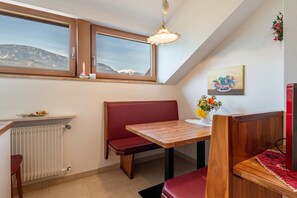 A room with a wooden table, red bench, and a window with a mountain view.