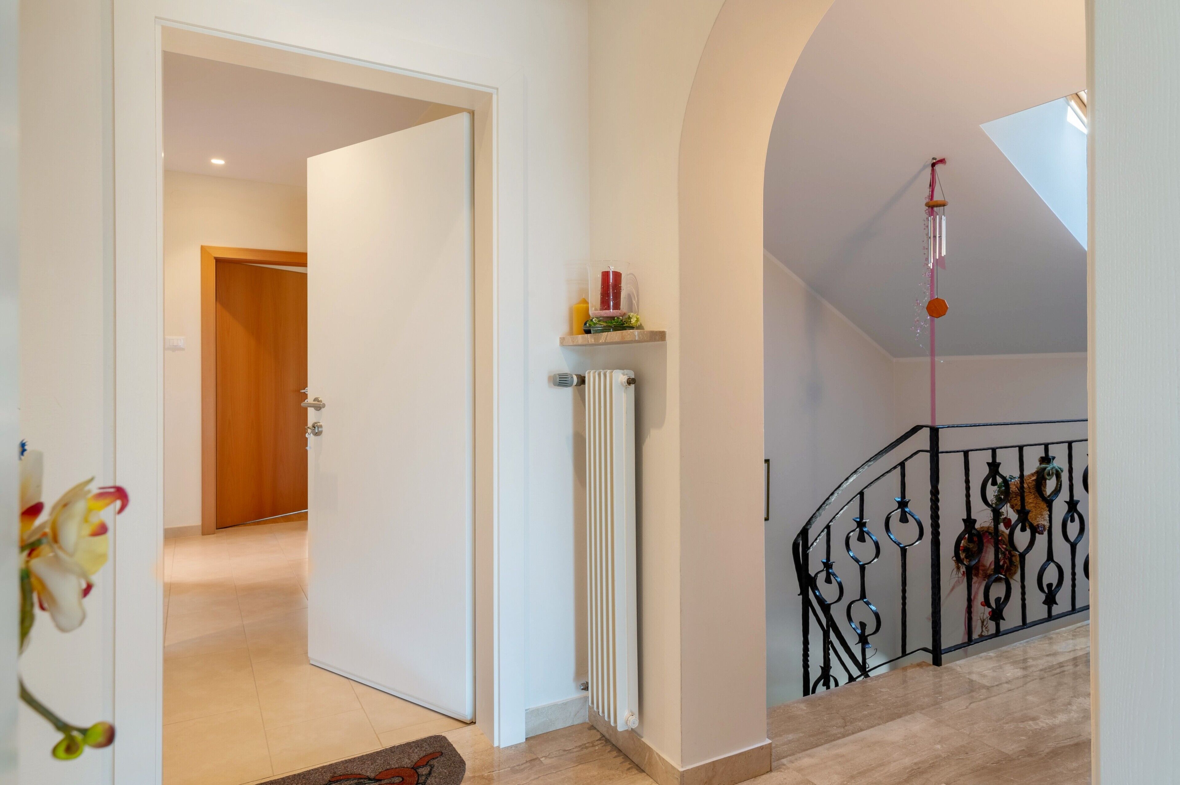 Un couloir avec une porte blanche, un radiateur et un escalier doté d’une rampe noire.