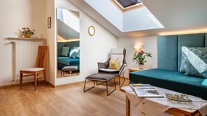 Ein modernes Wohnzimmer mit Dachfenster, einer Couch, einem Sessel, einem Tisch mit Büchern und einer Topfpflanze.