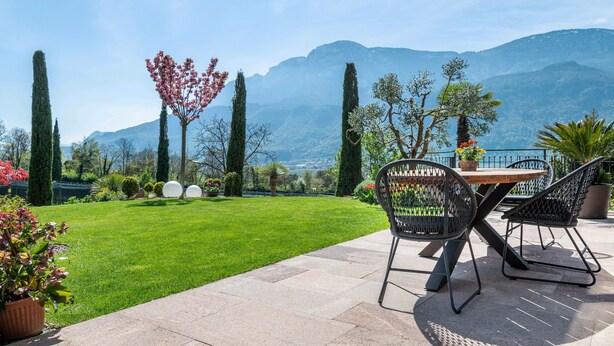 Eine Terrasse mit Tisch und Stühlen, ein gepflegter Rasen und Blick auf die Berge.
