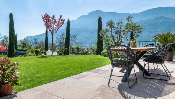 Een terras met een tafel en stoelen, een verzorgd gazon en een bergachtige achtergrond.