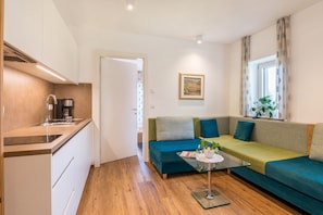 Un espace de vie compact comprenant un coin cuisine, un canapé, une table basse et une fenêtre avec des rideaux.