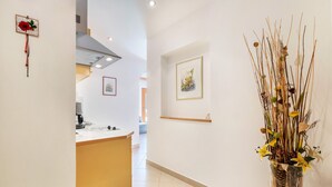Un couloir avec un coin cuisine, un tableau encadré au mur et une plante décorative.