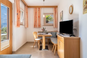 Une pièce comprenant une table à manger, des chaises, un téléviseur et une fenêtre avec des rideaux.