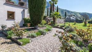 Un chemin pavé mène à un bâtiment doté d’un balcon qui offre une vue sur un paysage montagneux.
