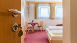 Une chambre d’hôtel avec une porte en bois, un lit, une petite table avec des chaises et une fenêtre avec des rideaux.
