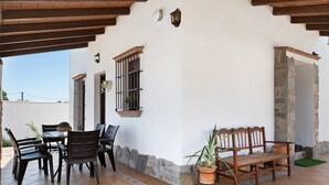 Ein überdachter Patio-Bereich mit Tisch und Stühlen, einer Holzbank und Kübelpflanzen.