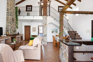A spacious living area with a stone fireplace, a sofa, a dining table, and a staircase leading to an upper level.