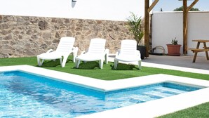 Ein Swimmingpool mit weißen Liegestühlen, einer Steinmauer und einer Pergola.