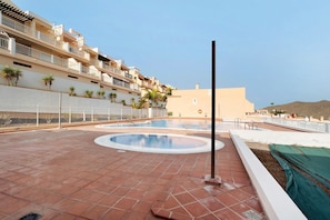 A rooftop swimming pool with a circular design, surrounded by a tiled deck and a low wall.