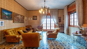 Una habitación con piso estampado, un sofá, sillones, una araña y una ventana con cortinas.