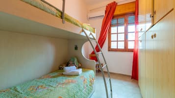 A bunk bed with a ladder, a chair, a stuffed toy, and a window with red curtains.
