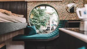 Ein kleiner Raum mit Etagenbett, rundem Fenster, einer blaugrünen Bank und einem kleinen Tisch.