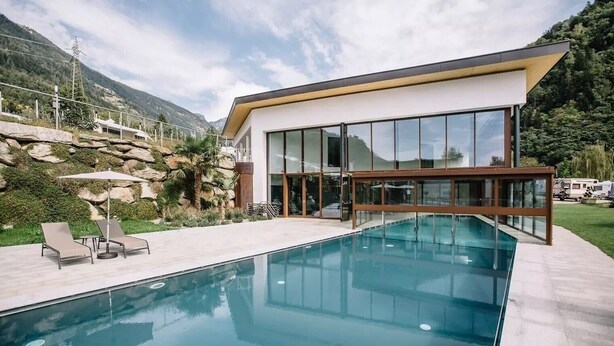 Ein modernes Haus mit Swimmingpool, großen Fenstern und Bergblick.