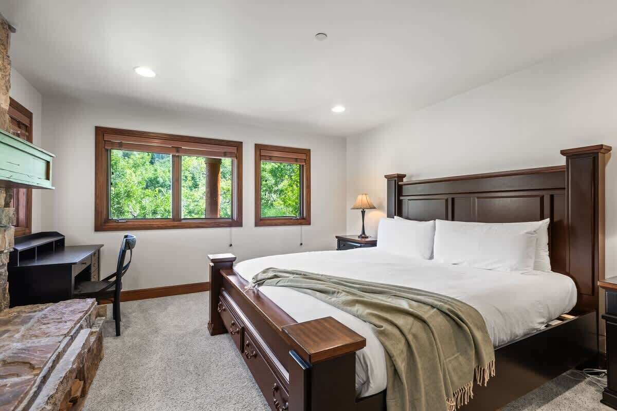 Une chambre avec un grand lit, deux fenêtres, un bureau et une lampe.